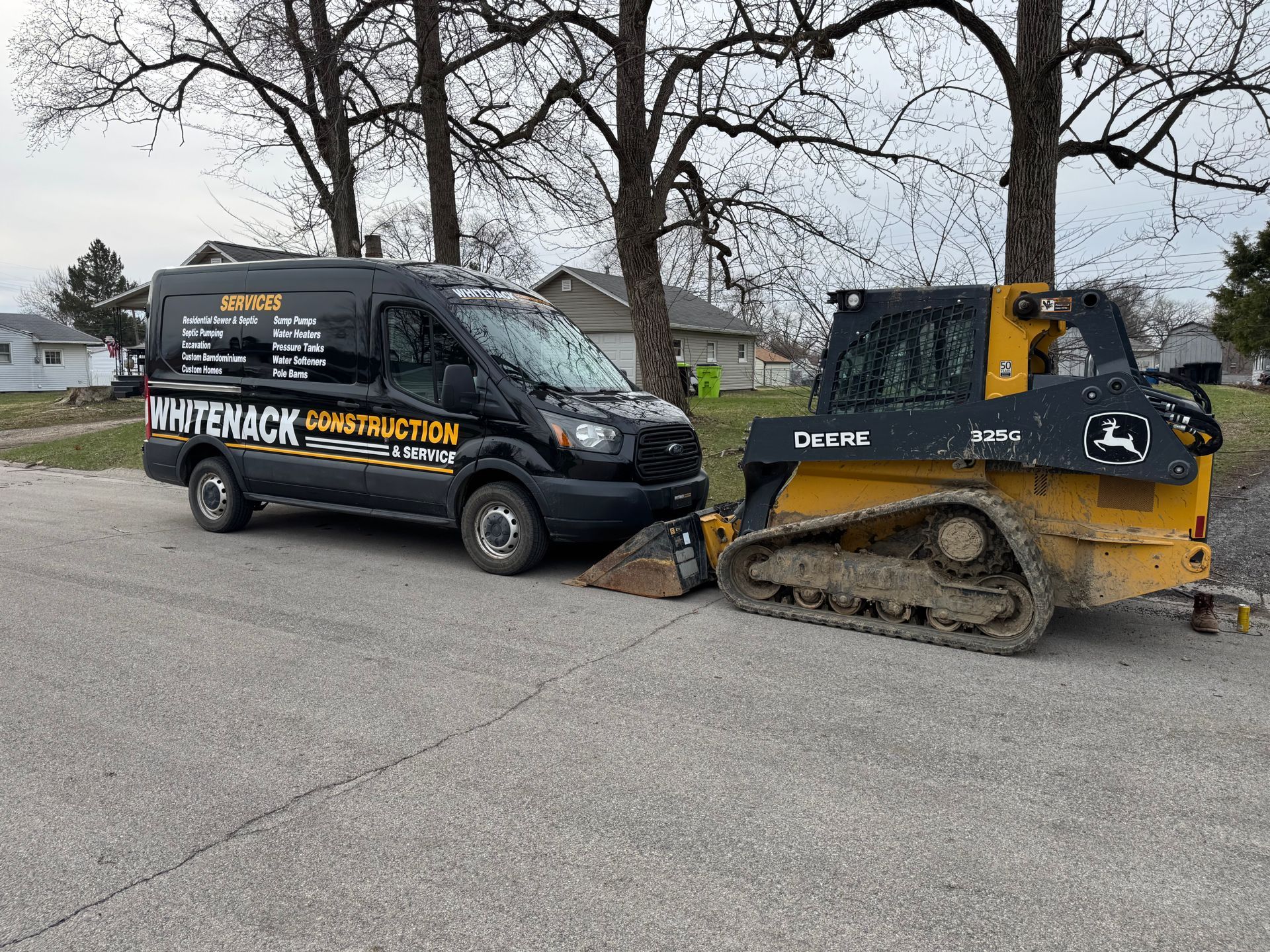 Black service van and yellow skid steer pushing dirt on a residential street.