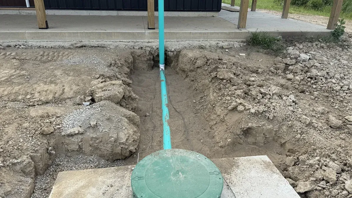 Turquoise pipe emerging from a dug-up dirt trench beside a concrete base outdoors