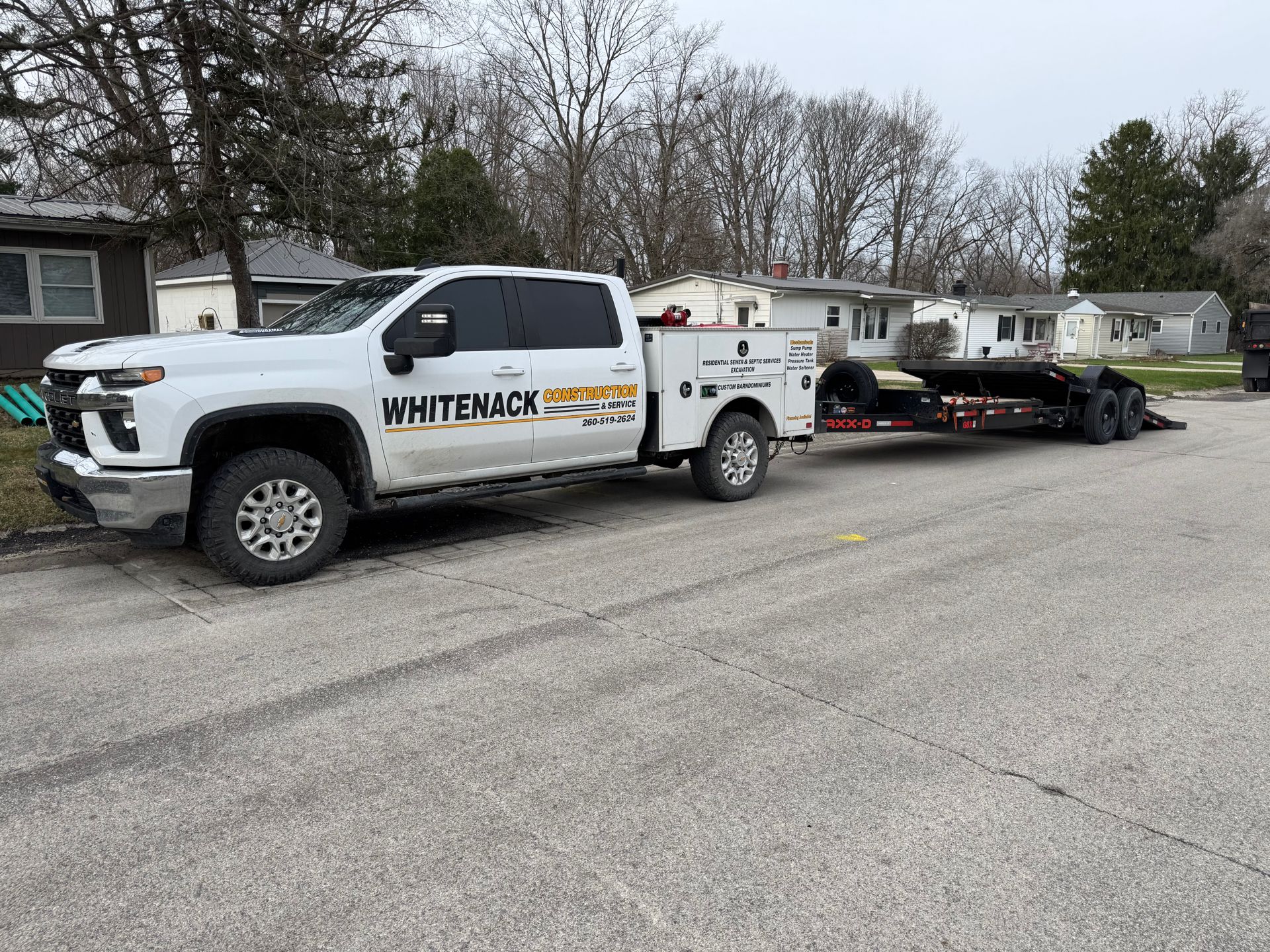 White truck towing a flatbed trailer with a small utility vehicle on a residential street