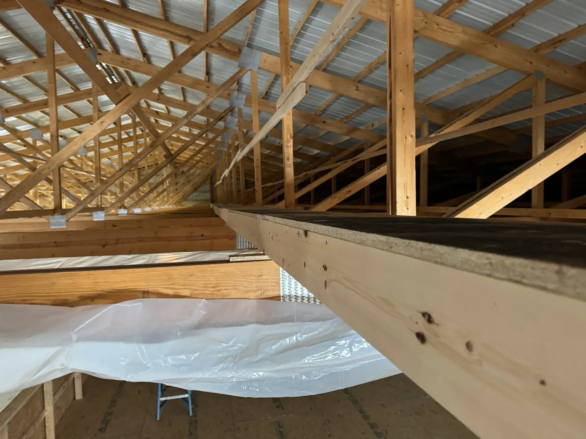 Interior of a wooden attic roof truss under construction, with exposed beams and white plastic sheeting below