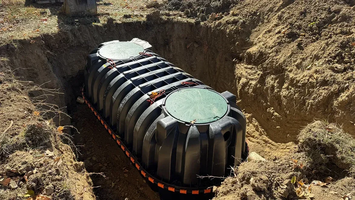 Black cylindrical tank buried in a dirt trench at a construction site, with a green cap on top.