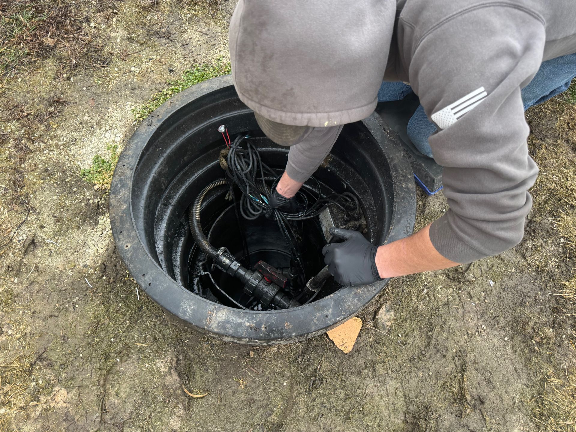 Person crouched over an open utility pit, handling cables inside a black plastic chamber.