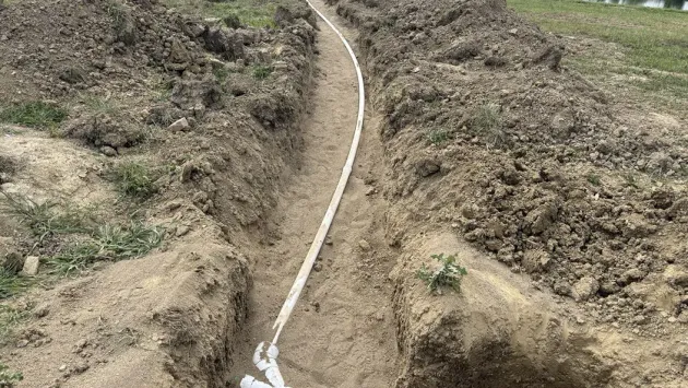 White pipe runs through a dry, rocky dirt trench on a hillside.