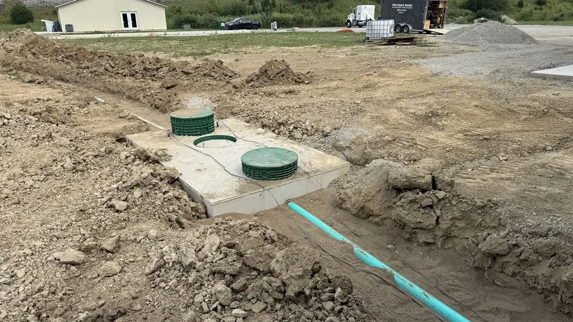 Construction site with exposed trenches and green utility covers in muddy dirt