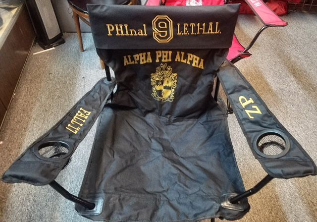 A black folding chair with alpha phi alpha written on it