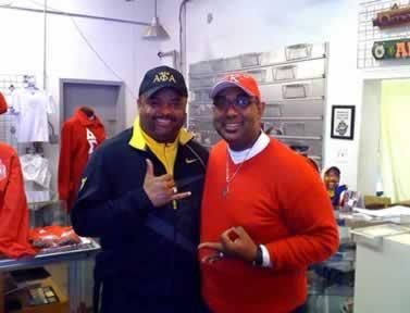 Two men are posing for a picture in a store with one wearing a hat that says ata