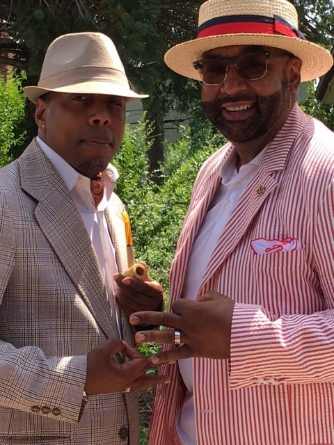 Two men wearing suits and hats are standing next to each other