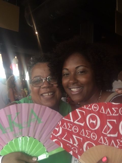 Two women are posing for a picture and one has a fan with the letter s on it