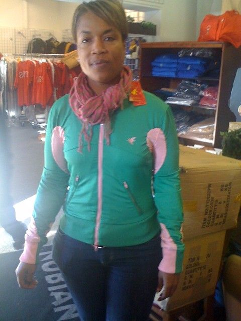 A woman in a green and pink jacket stands in front of a sign that says indian