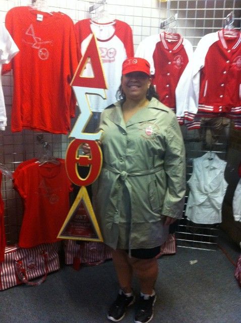 A woman in a trench coat stands in front of a display of red shirts