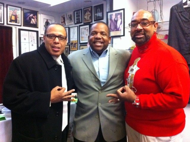 Three men posing for a picture in a room with pictures on the wall