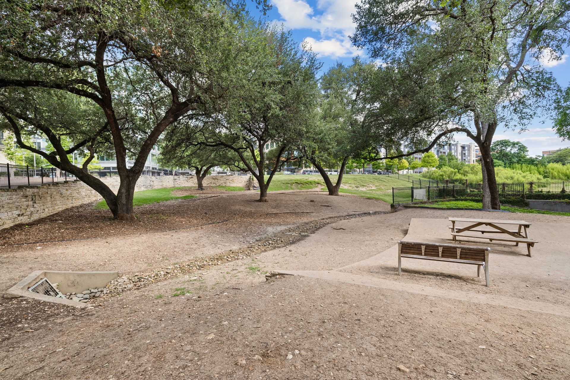Park with large trees, gravel paths, and picnic tables under a blue sky at Sabina in Austin, TX.