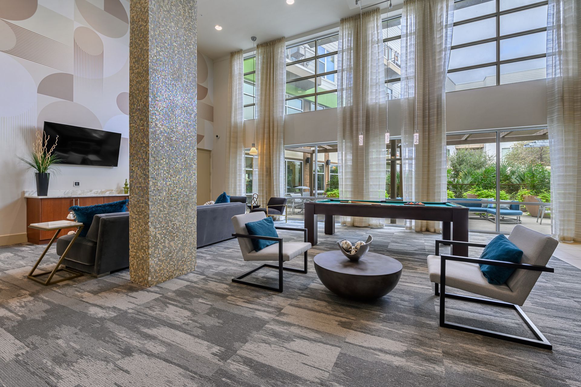 Spacious modern lounge area with pool table, large windows, couches, armchairs, and patterned carpet at Sabina, offering apartments in Central Austin, TX.