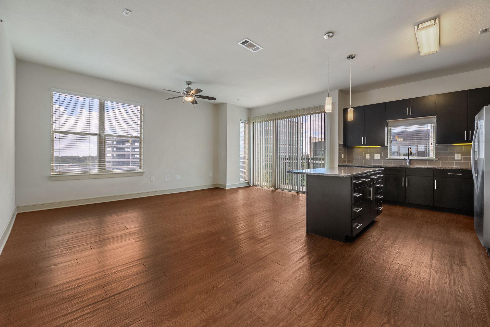 Open-concept apartment with hardwood floors, dark cabinets, an island, and large windows at Sabina, offering affordable apartments in Austin, TX.