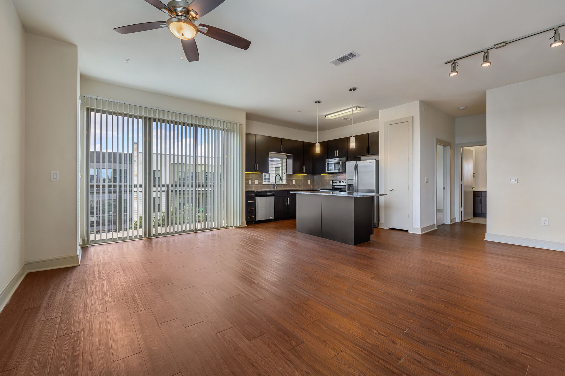 Empty apartment with dark wood floors, kitchen, balcony, and ceiling fan at Sabina, offering affordable apartments in Austin, TX.