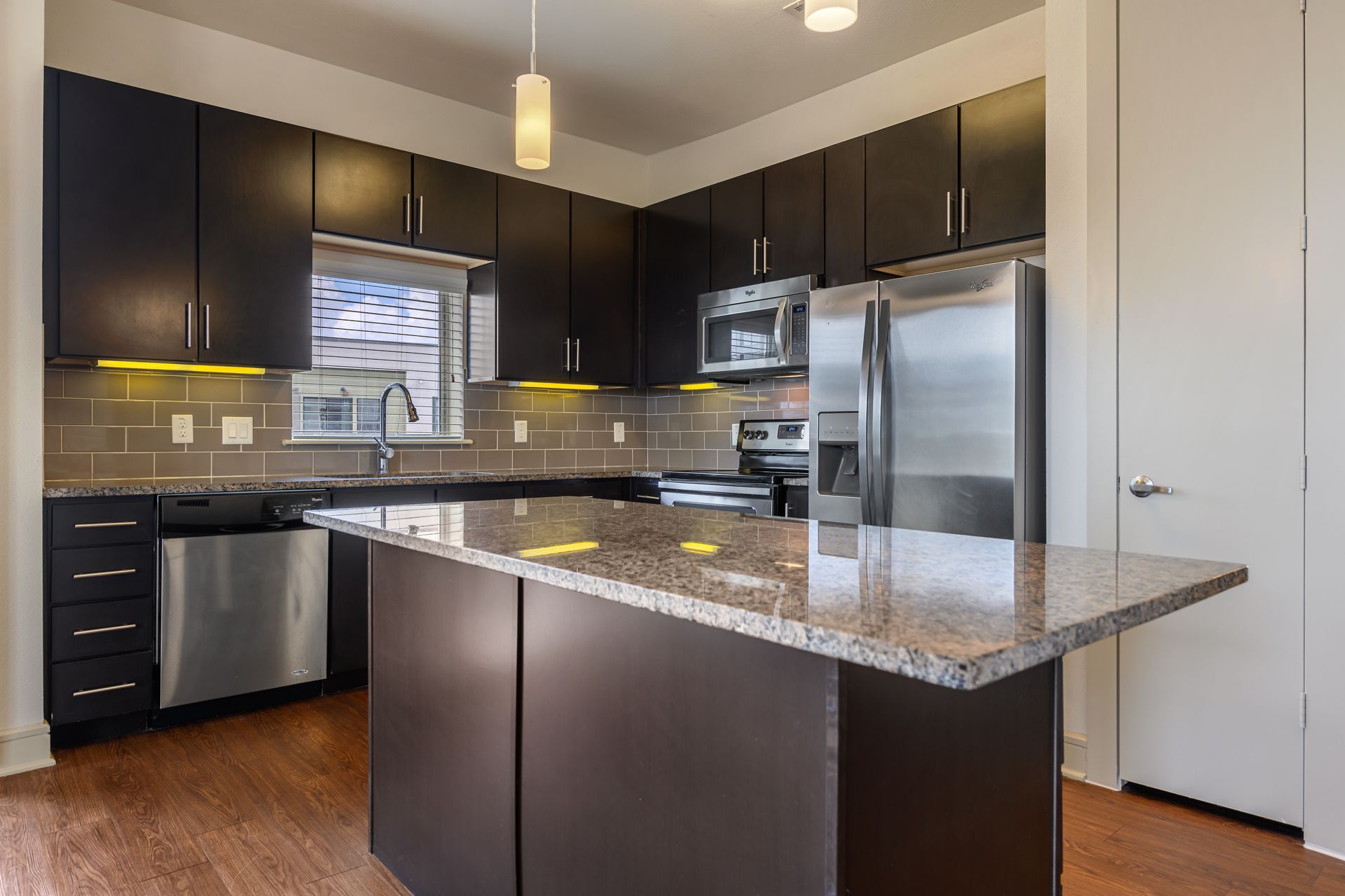 Modern kitchen with dark brown cabinets, stainless steel appliances, and granite island at Sabina, offering apartments near Zilker Park Austin.