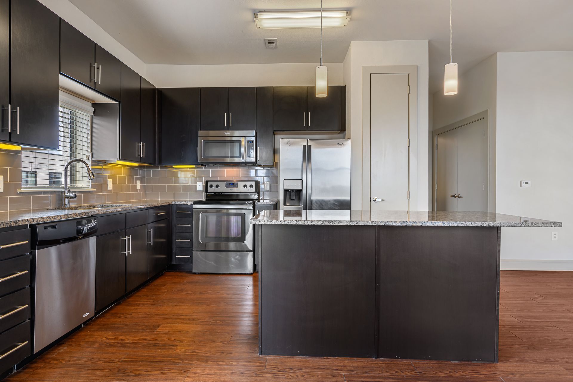 Modern kitchen with dark cabinets, stainless steel appliances, and island with granite countertop at Sabina, offering affordable apartments in Austin, TX.