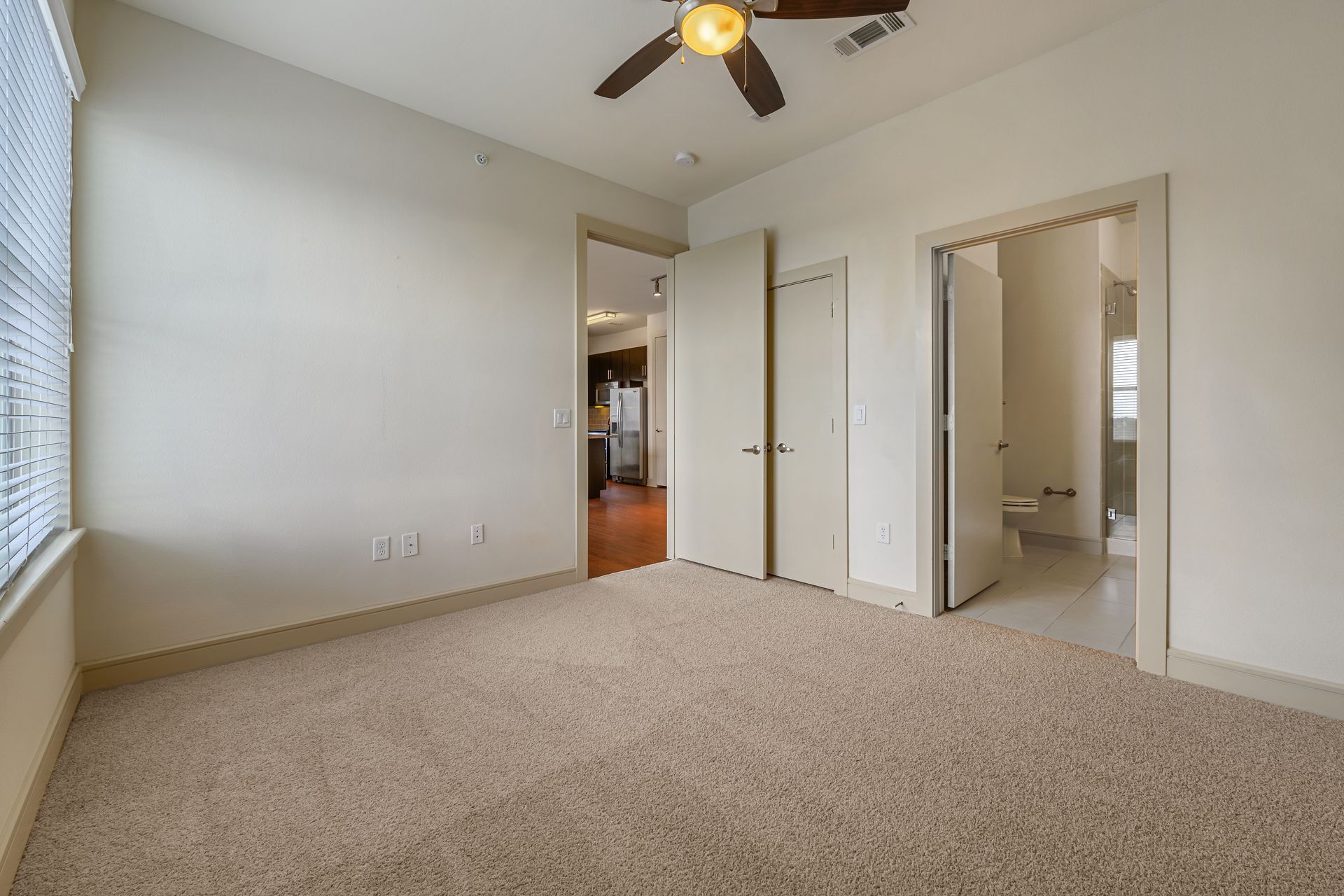 Empty bedroom with beige carpet, open doors, and a ceiling fan at Sabina, offering affordable apartments in Austin, TX.