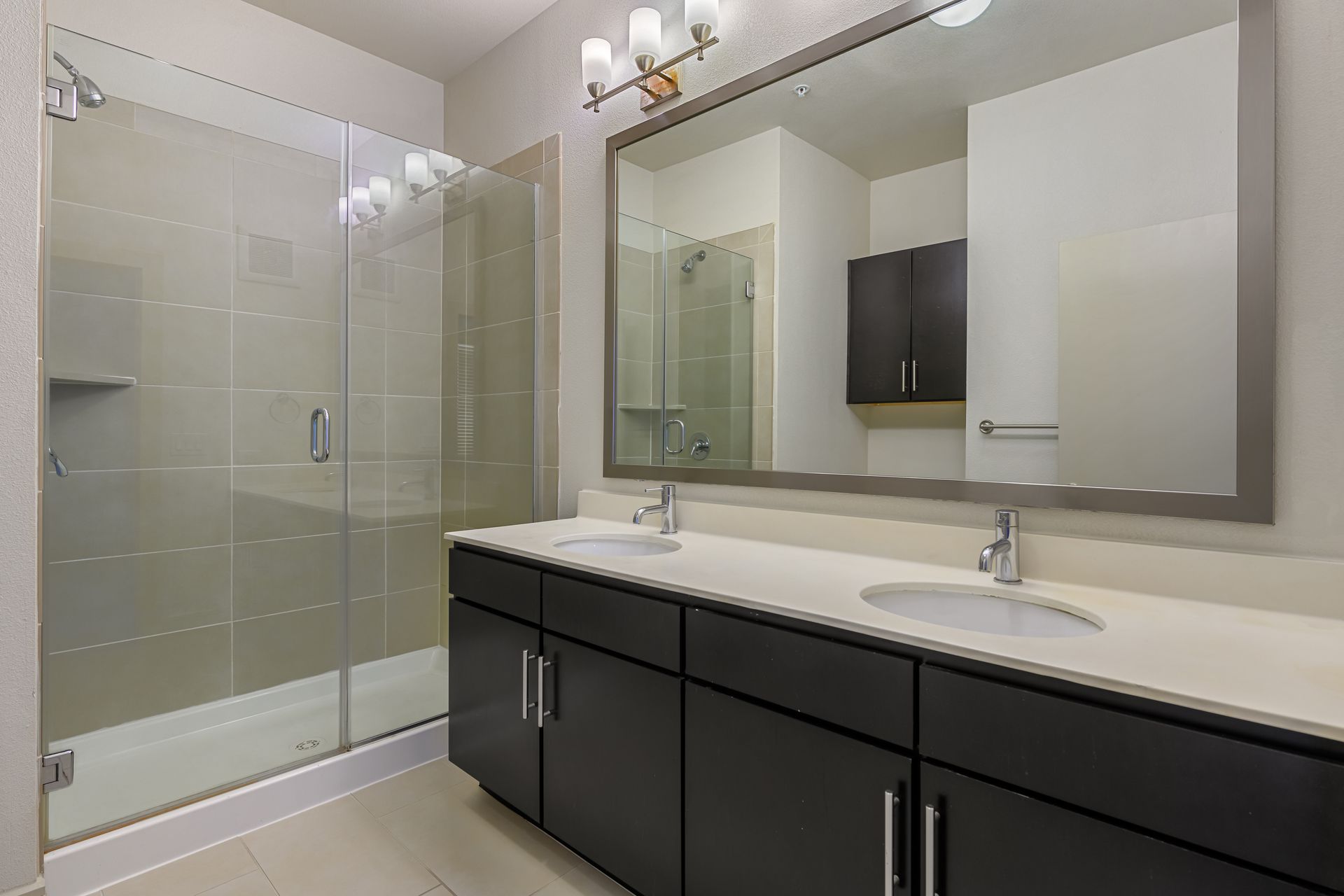 Modern bathroom with a glass shower, double sinks, and dark cabinetry at Sabina, offering affordable residences in Central Austin, TX.