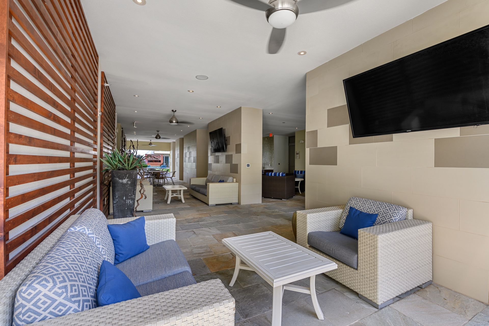 Outdoor patio with wicker furniture, a TV, and a slatted wooden wall at Sabina, offering pet-friendly apartments in Central Austin, TX.