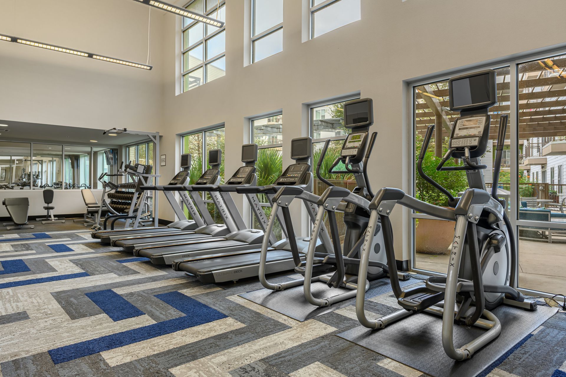 Gym with treadmills and elliptical machines, near a large window at Sabina, offering pet-friendly apartments in Central Austin, TX.