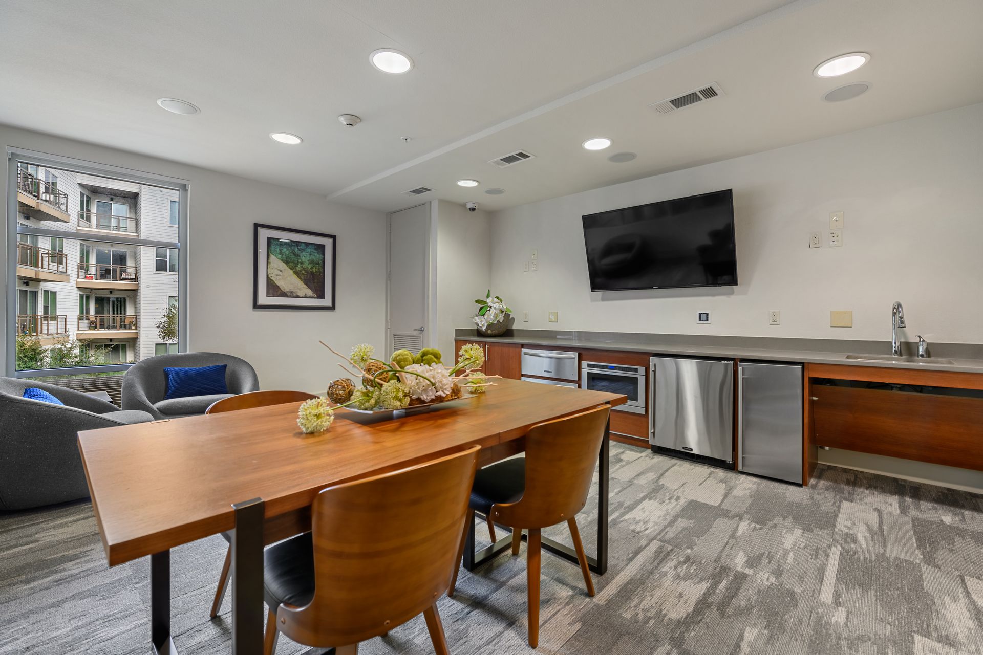 Community lounge with table, chairs, kitchen appliances, TV, and a window at Sabina, offering apartments near Downtown Austin, TX.