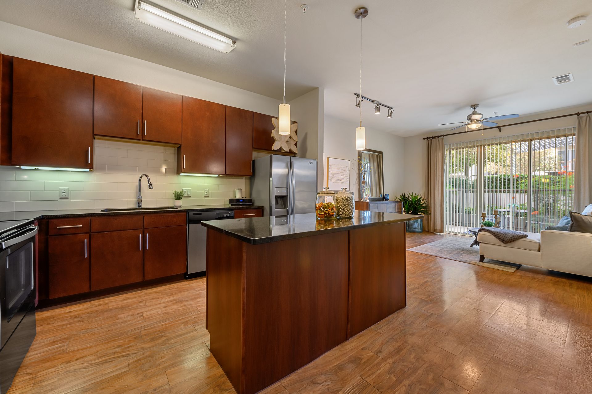 Kitchen with wood cabinets, island, stainless steel appliances, and open to a living area with patio doors at dusk at Sabina, offering apartments in Austin Near UT.