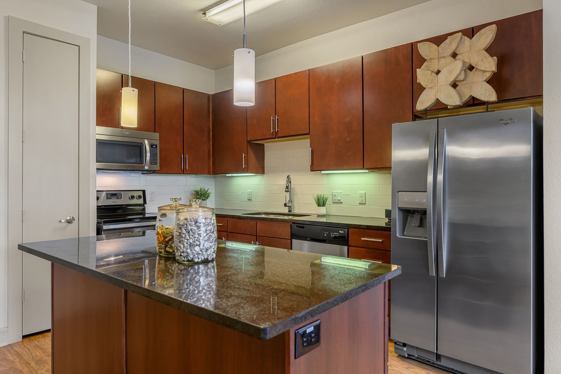Modern kitchen with stainless steel appliances, dark wood cabinets, and a granite island at dusk at Sabina, offering apartments in Austin Near UT.