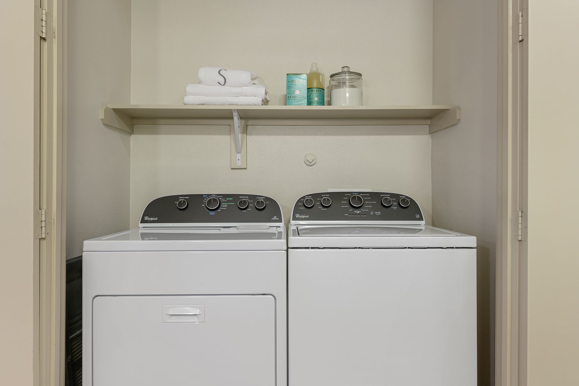 Laundry room with white washer and dryer, shelf with towels and toiletries at Sabina, offering apartments with in unit washer and dryer in Central Austin, TX.