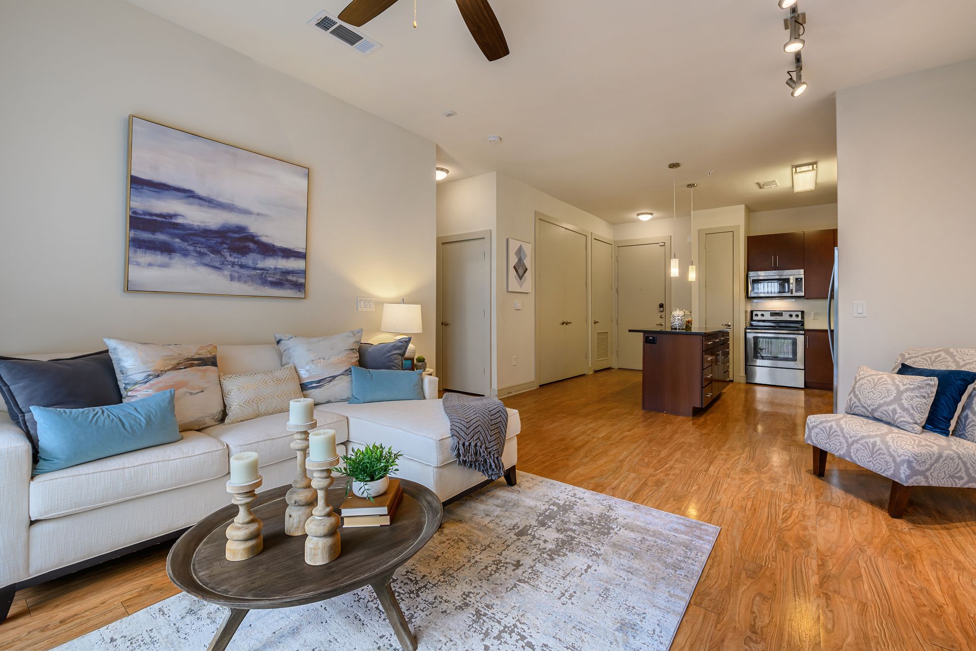 Living room with a white sofa, coffee table, and open kitchen, with hardwood floors and artwork at dusk at Sabina, offering apartments near Zilker Park Austin.