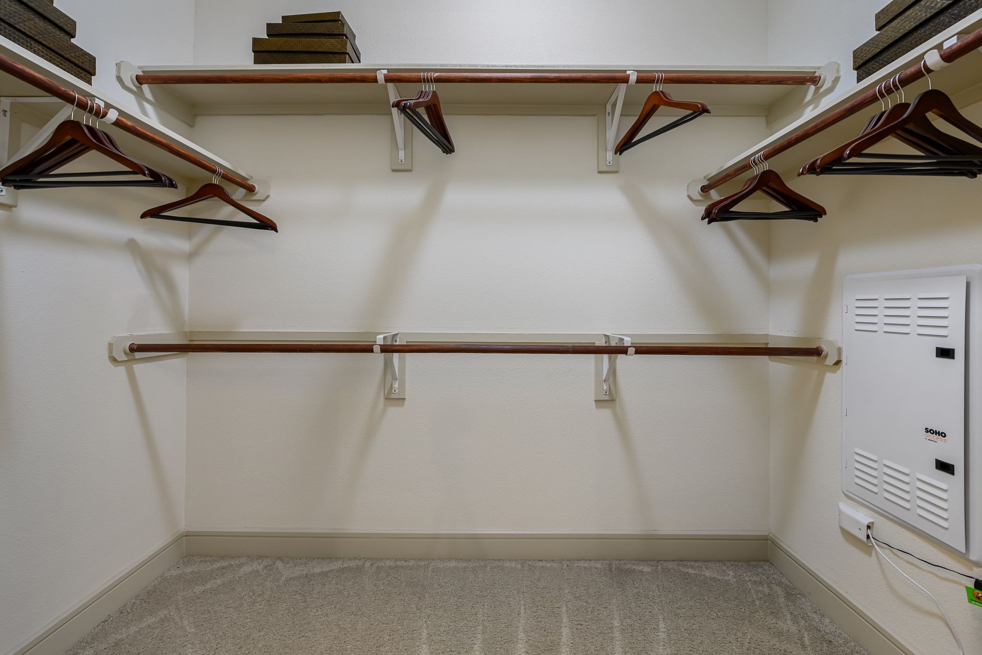 Empty white closet with shelves, hanging rods, and dark wooden hangers at Sabina, offering affordable residences in Central Austin, TX. Boxes on top shelf.