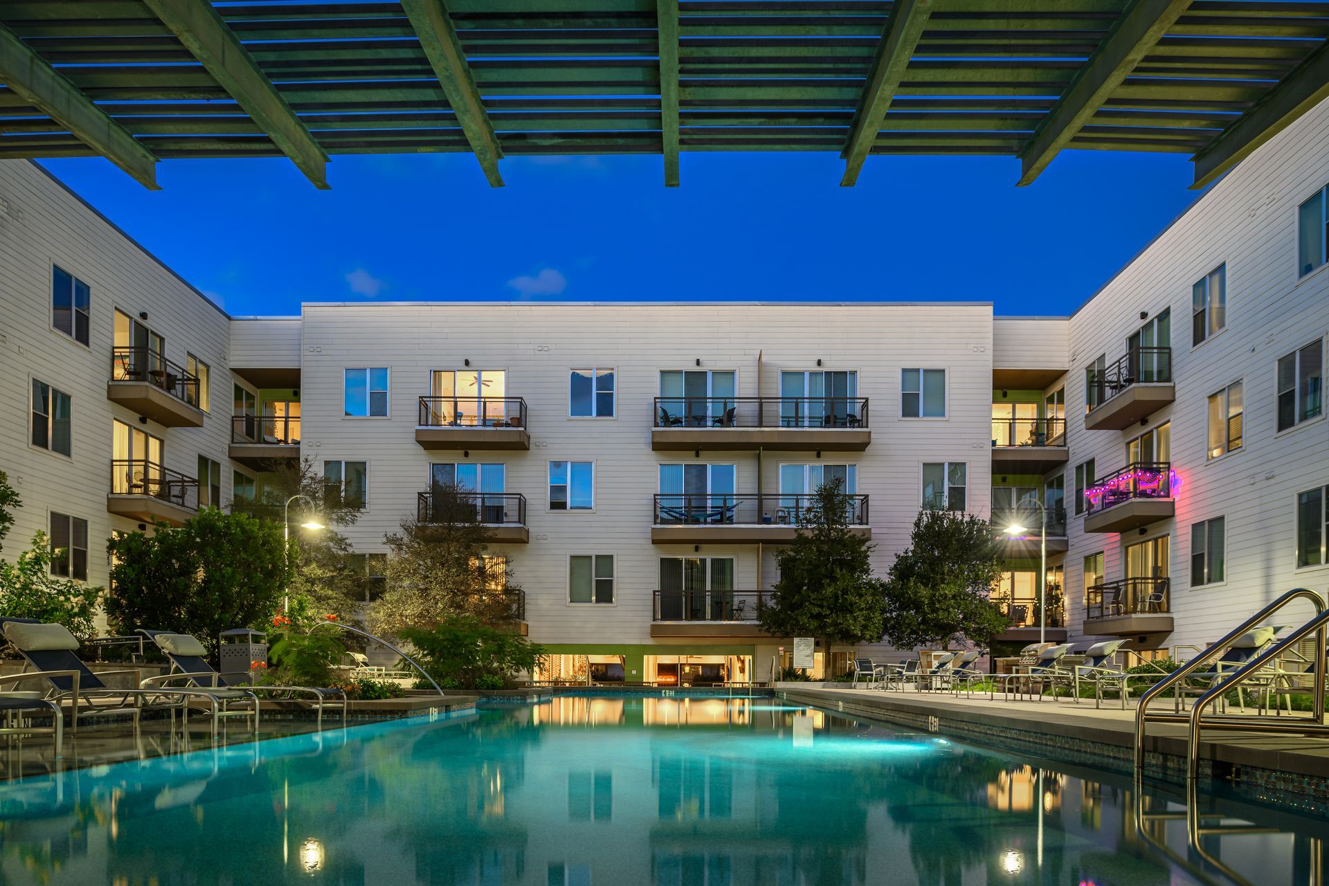 Swimming pool in a courtyard with a four-story building in the background at dusk at Sabina, offering apartments in Austin Near UT. Blue sky above.