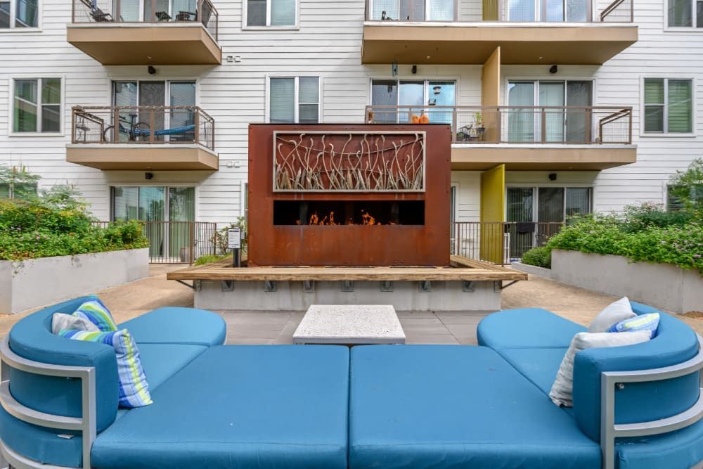 Outdoor fireplace with a large blue couch is sitting in front of the apartment building at Sabina in Austin, TX.