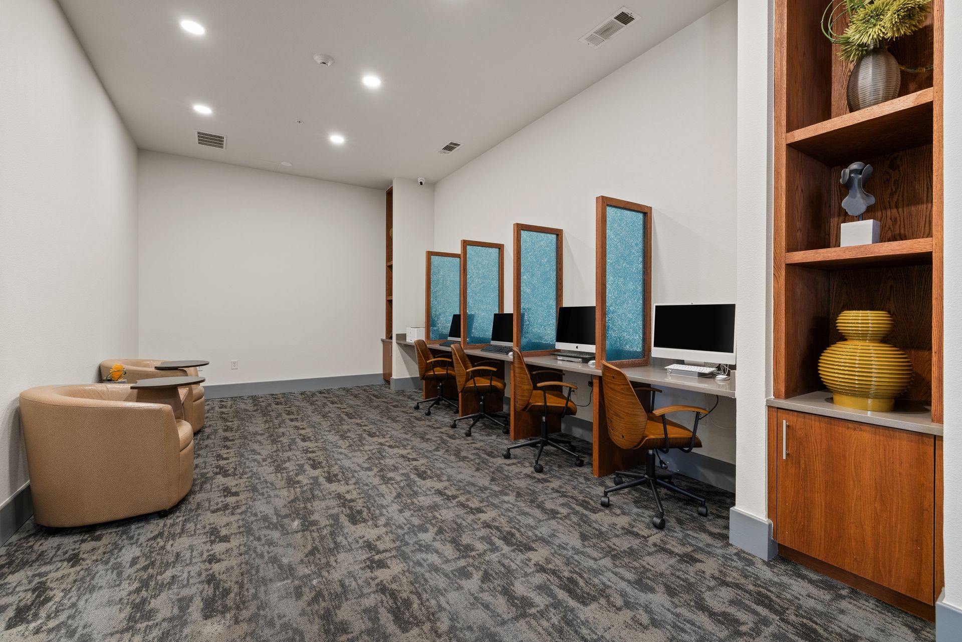 Modern office lounge with workstations, blue chairs, carpet, and wooden shelving at Sabina in Austin, TX.