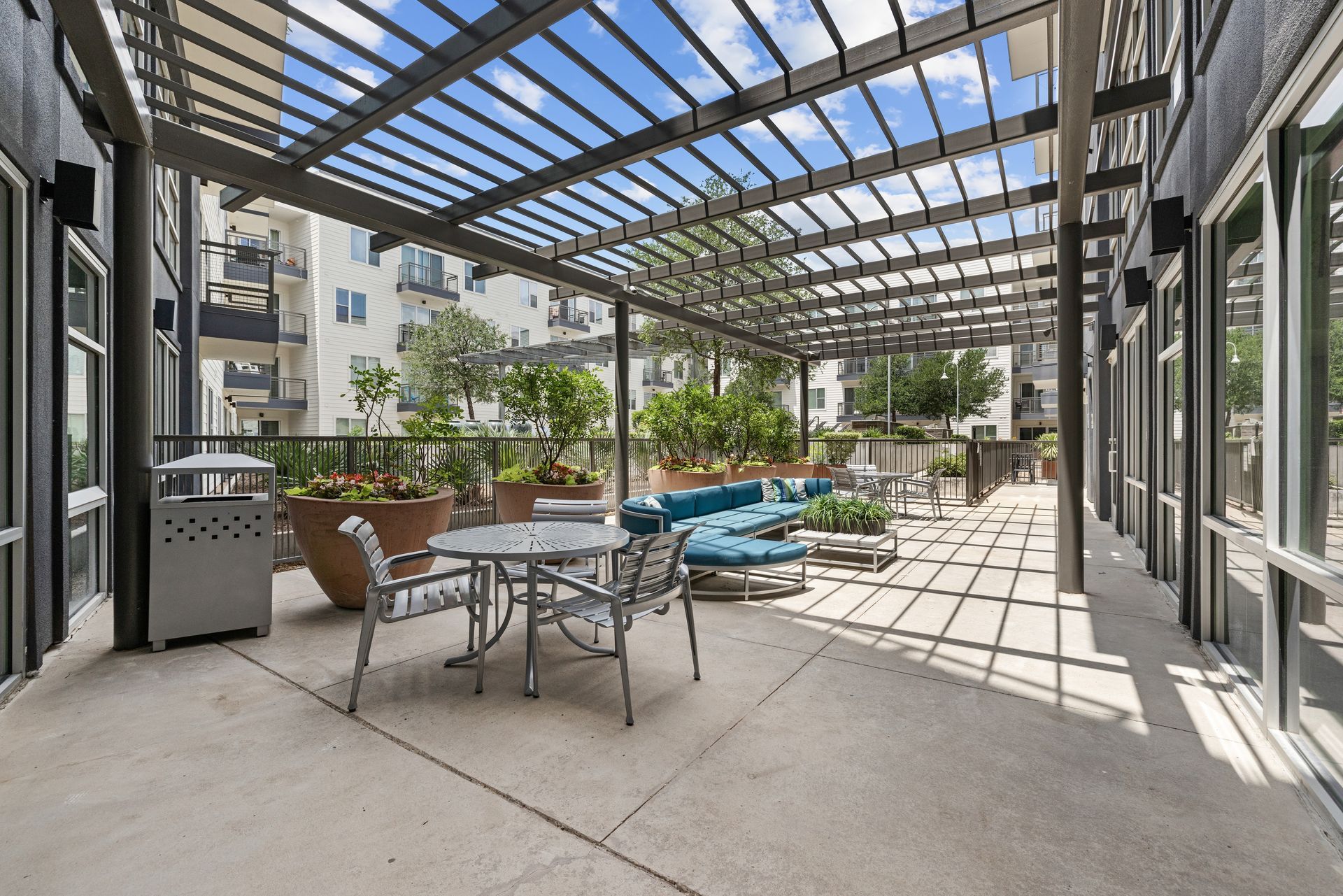 Covered patio with outdoor seating, striped awning, and potted plants in bright sunlight at Sabina in Austin, TX.