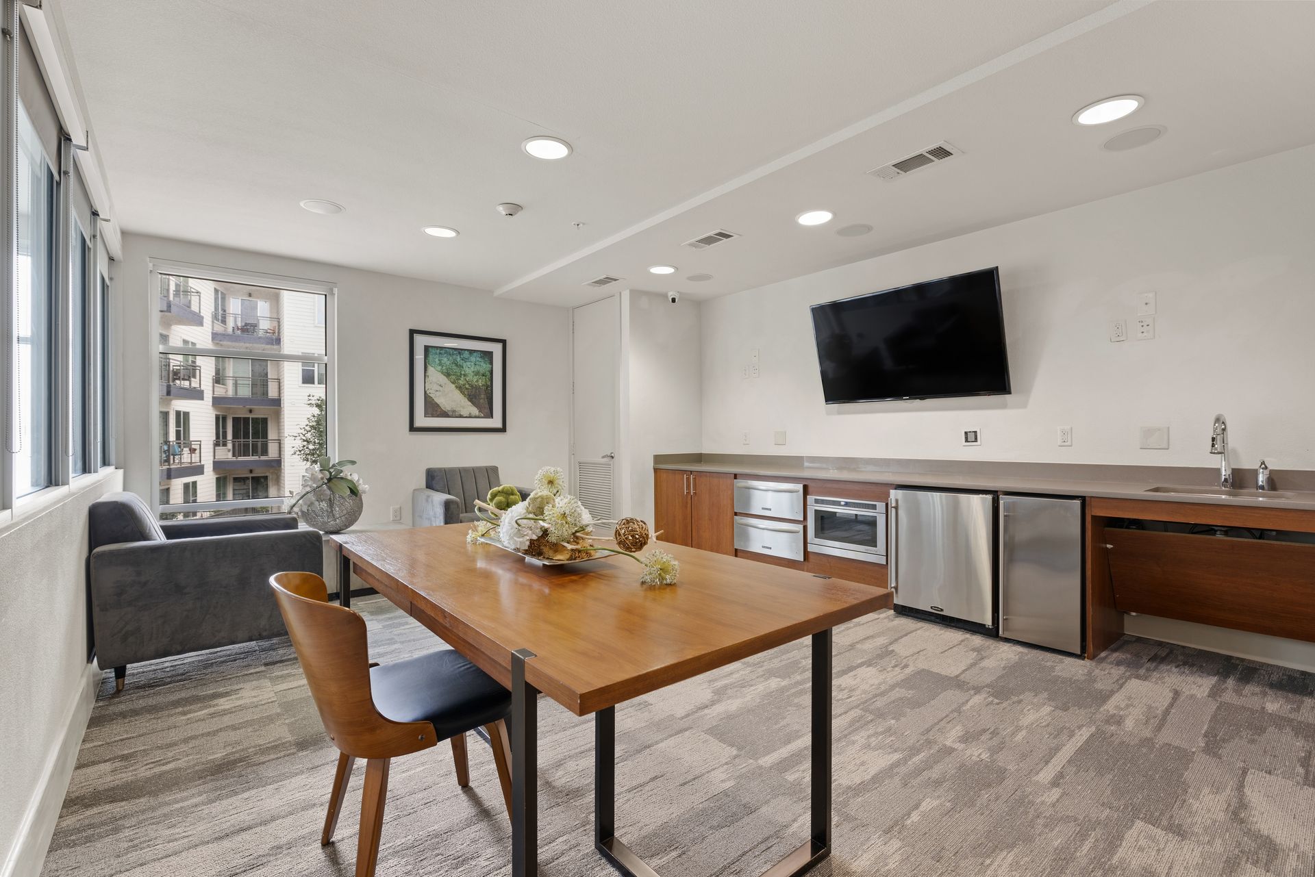 Modern open-plan clubroom with wood table, TV, kitchenette, and city-view windows at Sabina in Austin, TX.