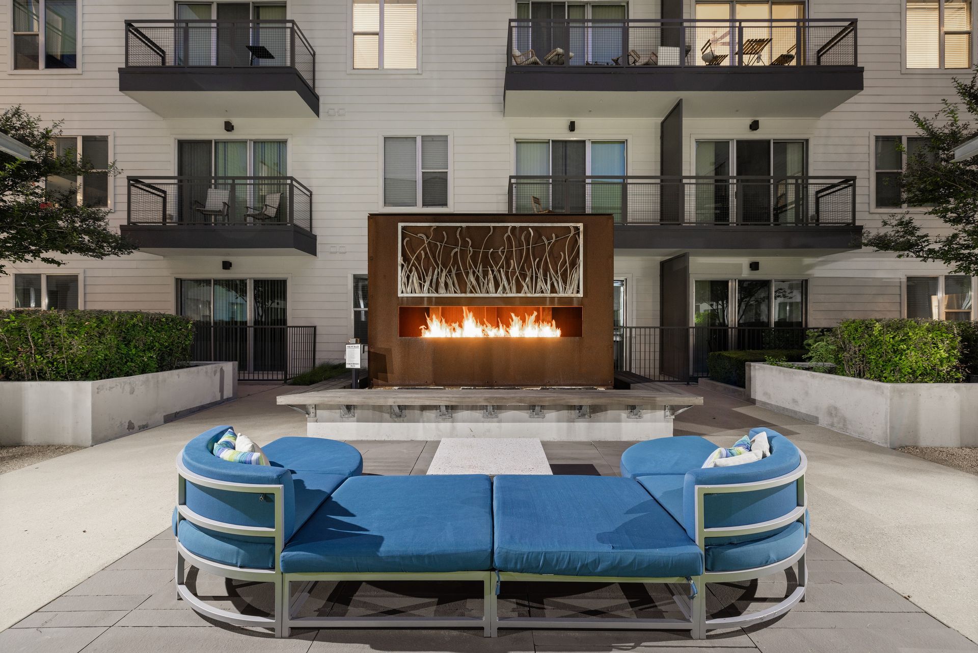 Modern apartment courtyard with blue daybed seating and a lit outdoor fireplace at Sabina in Austin, TX.