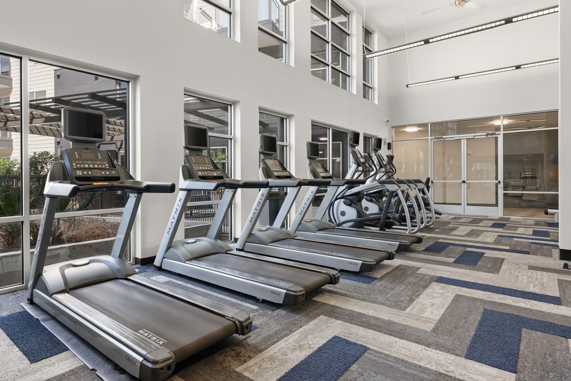 Modern gym with treadmills, weight machines, and large windows in a bright carpeted room at Sabina in Austin, TX.