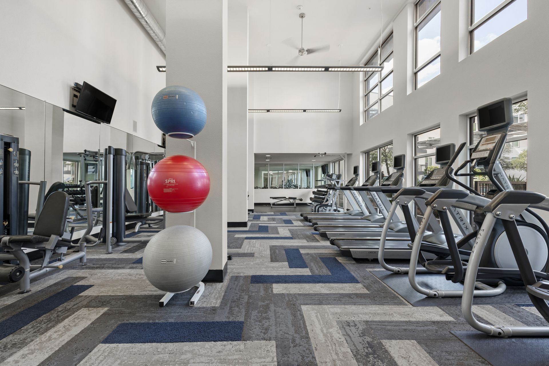 Bright modern gym with treadmills, mirrors, and exercise balls stacked by a white column at Sabina in Austin, TX.