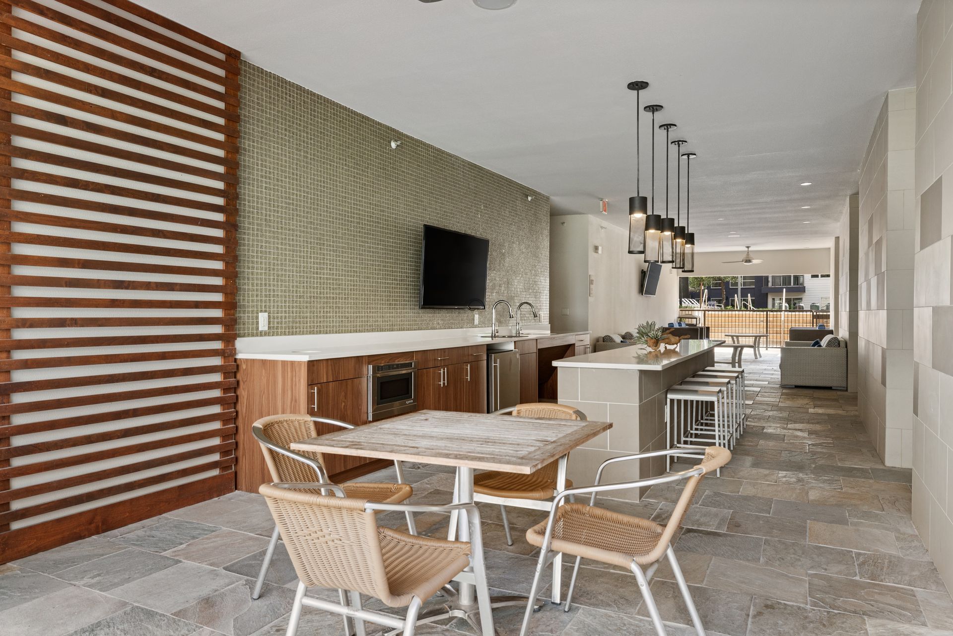 Modern outdoor dining area with tables, chairs, bar stools, and a wall-mounted TV at Sabina in Austin, TX.