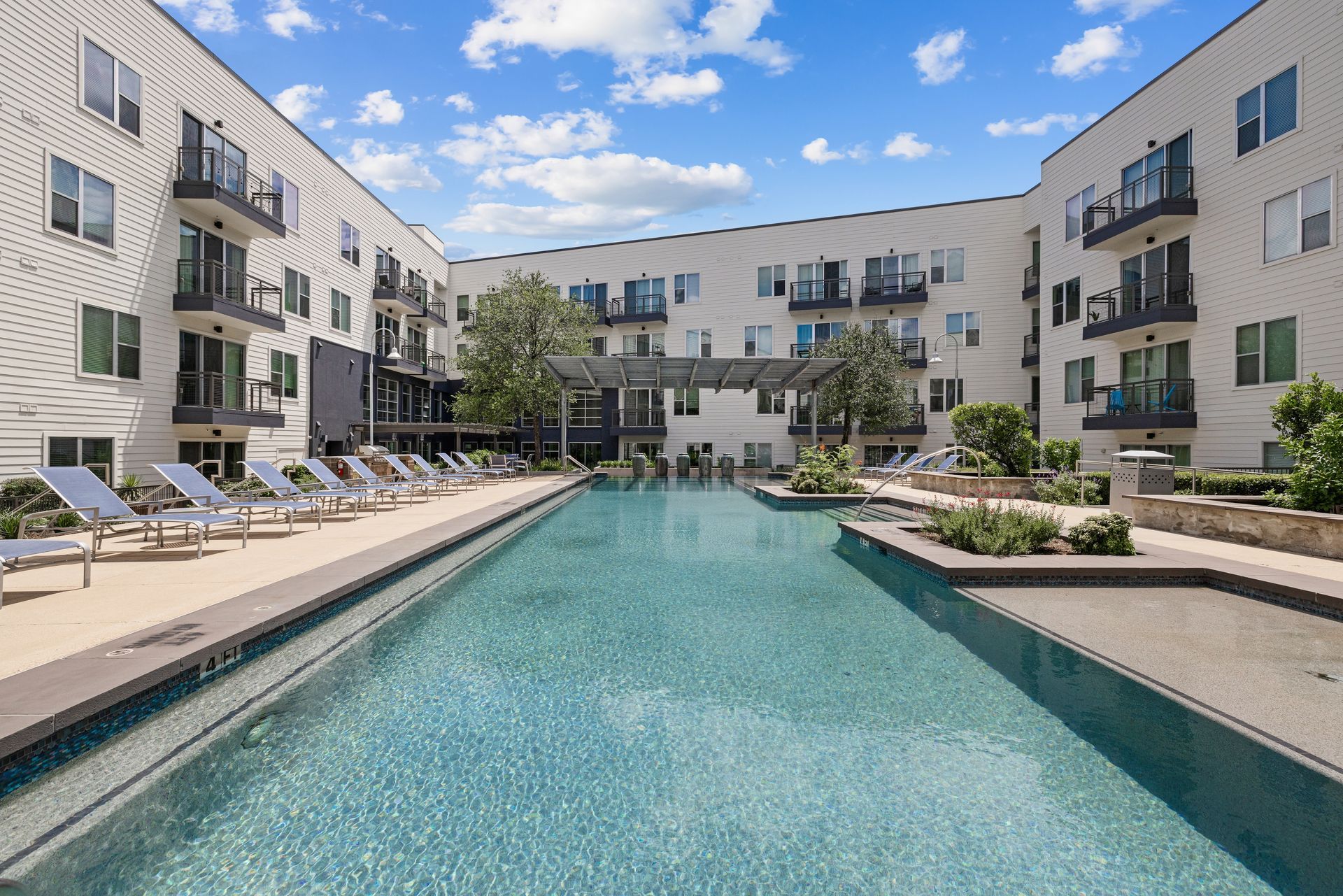 Modern apartment courtyard with a long turquoise swimming pool and lounge chairs on both sides at Sabina in Austin, TX.