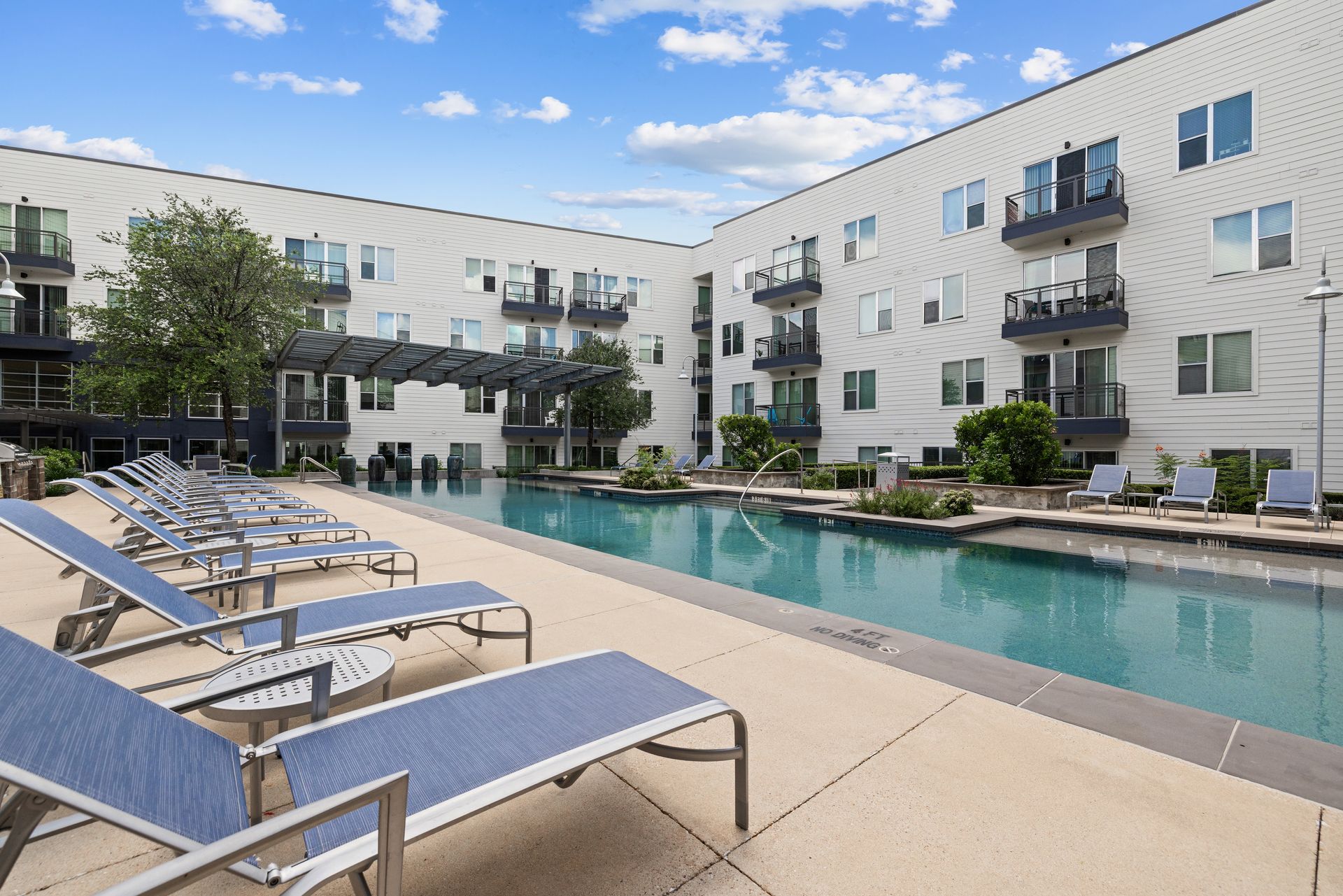 Apartment complex pool with lounge chairs and modern buildings under a blue sky at Sabina in Austin, TX.