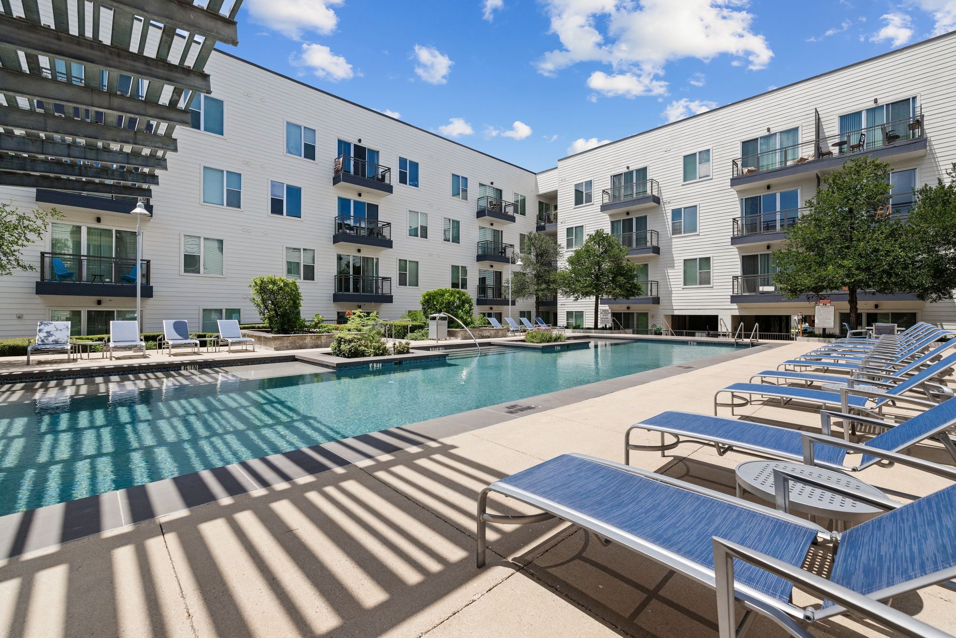 Modern apartment courtyard with a swimming pool, lounge chairs, and balconies under a sunny sky at Sabina in Austin, TX.