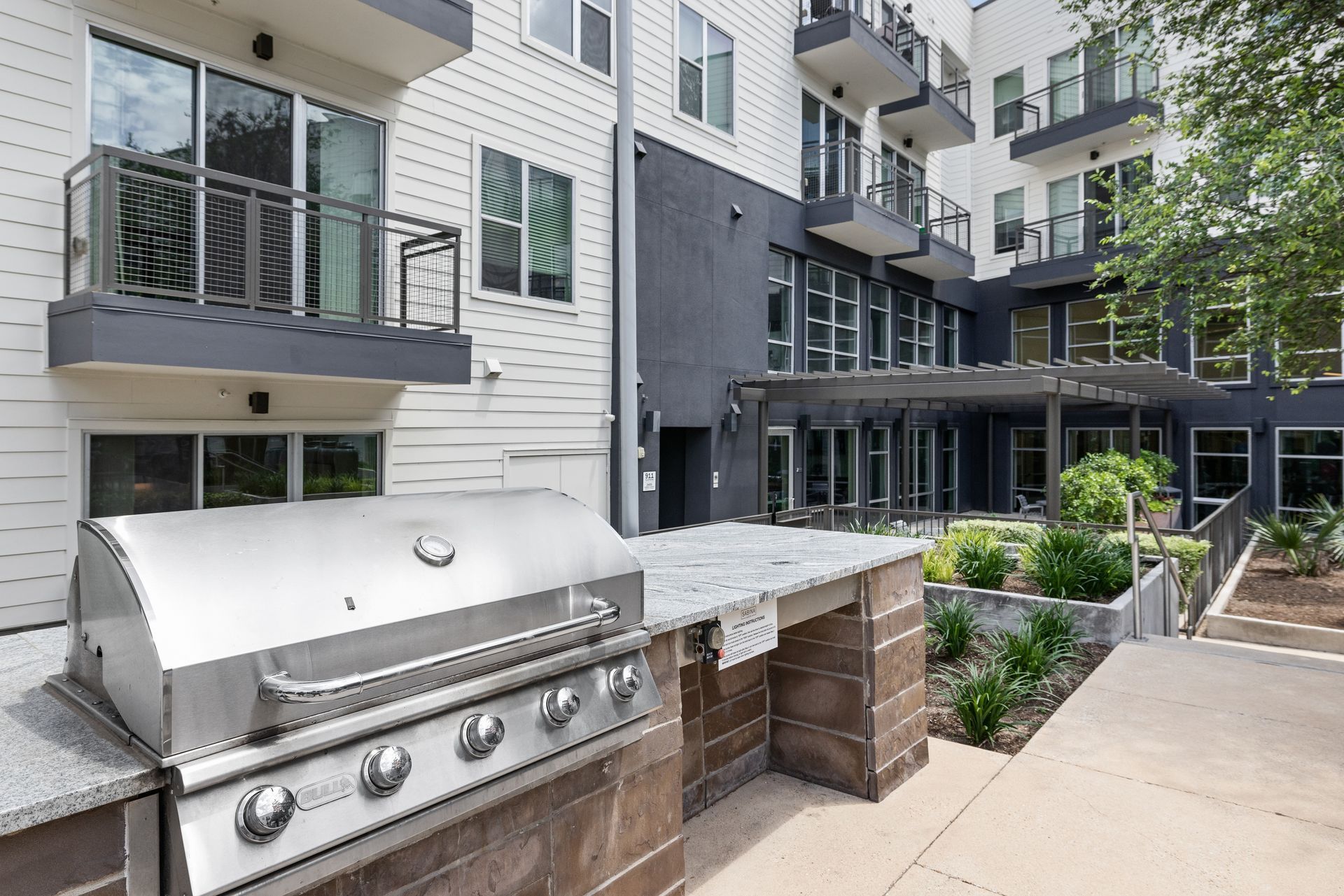 Apartment courtyard with stainless steel grills, landscaped planters, and balconies at Sabina in Austin, TX.