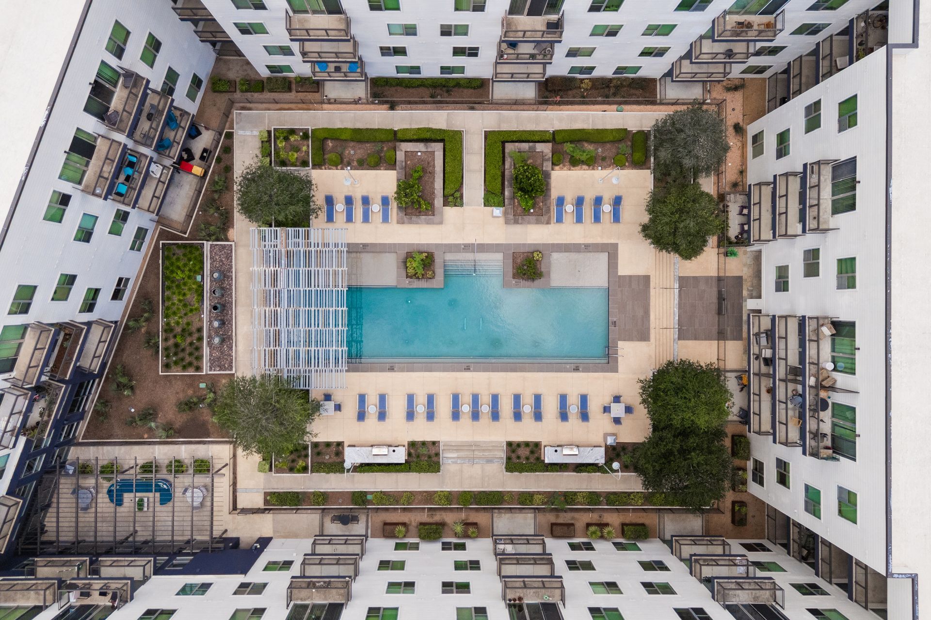 Aerial view of a courtyard pool surrounded by white apartment buildings, lounge chairs, and greenery at Sabina in Austin, TX.
