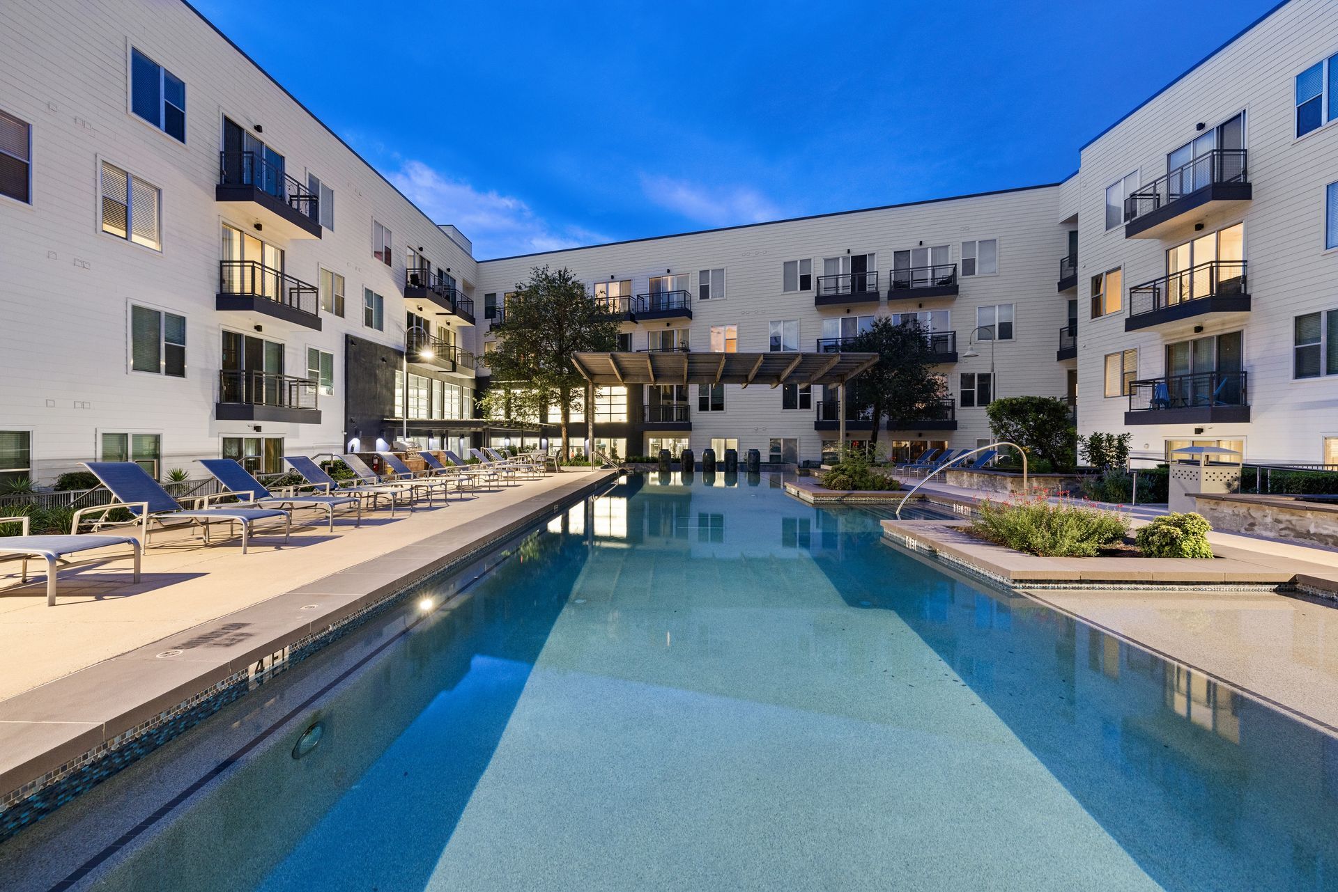 Modern apartment courtyard with a blue swimming pool at dusk at Sabina in Austin, TX.