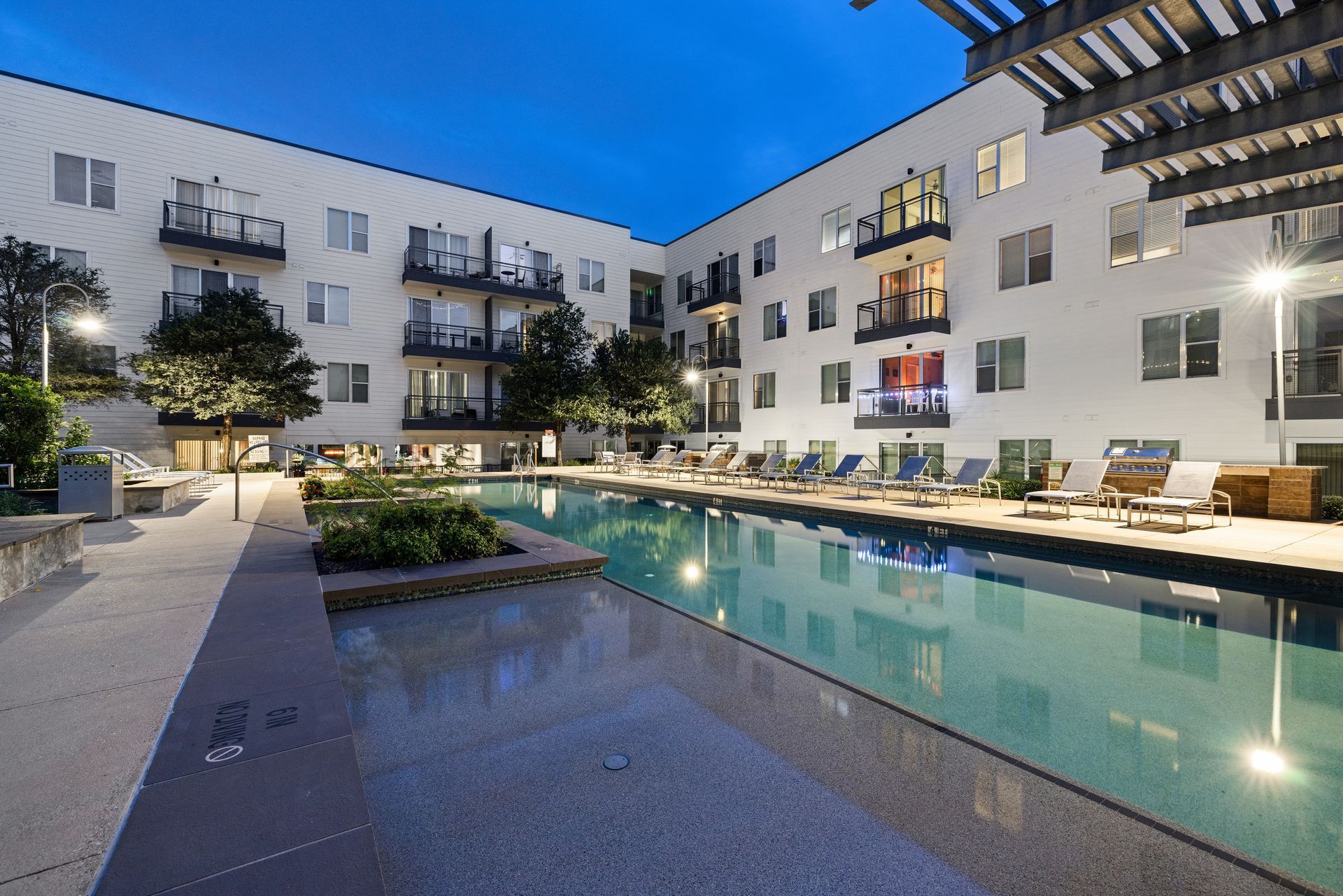 Modern apartment courtyard with lit swimming pool at dusk at Sabina in Austin, TX.