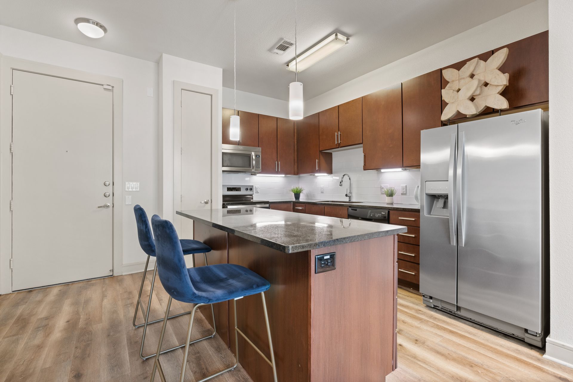 Modern kitchen with stainless steel appliances, wood cabinets, island, and two blue bar stools at Sabina in Austin, TX.