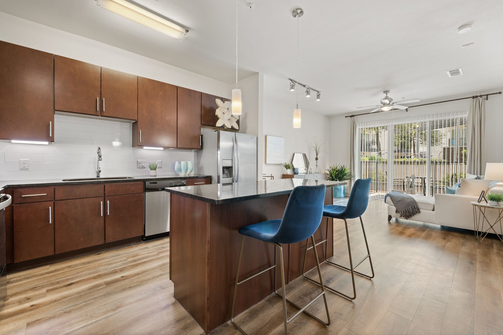 Modern kitchen and living area with wood cabinets, breakfast bar, blue stools, and large sliding glass doors at Sabina in Austin, TX.