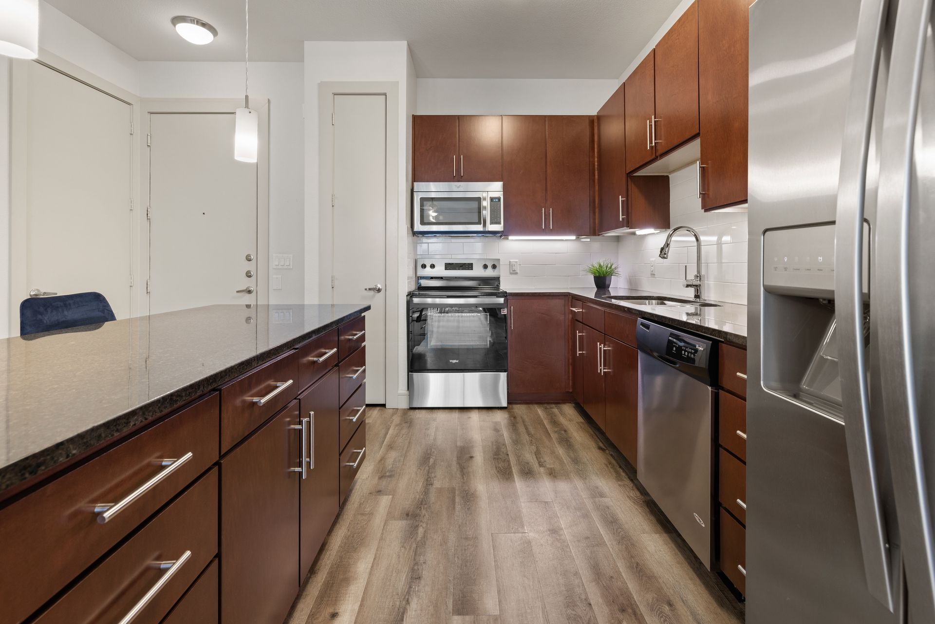 Modern kitchen with stainless steel appliances, wood cabinets, black countertops, and wood-look flooring at Sabina in Austin, TX.